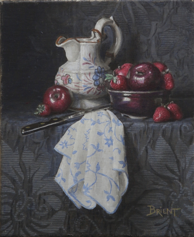 Pichet blanc, un bol de pommes et de fraises,  une serviette à motifs sur un tissu bleu  