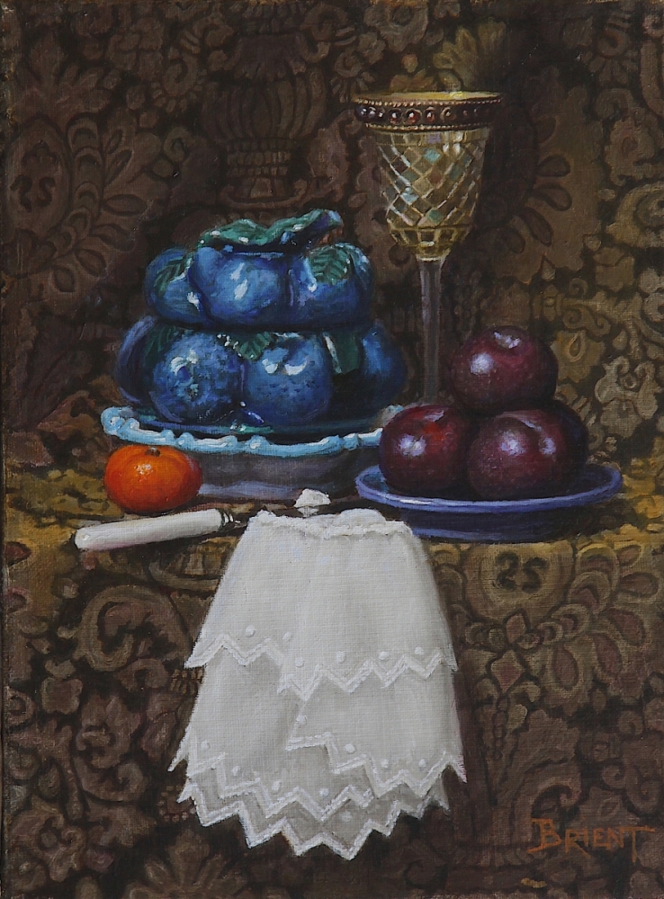A Covered bowl of blue barbotine, a glass made of mosaiic, a plate of dark plums, a clementine on a pattern fabric